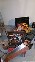 Overview of the toolbox open showing screwdrivers, wrenches, pliers and Dewalt power tools behind it including drills and saws with yellow accents, an extension cord and battery charger.