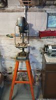 Full view of the Toolkraft 350B drill press mounted on an orange stand in a workshop basement environment.