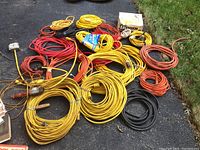 Multiple coiled extension cords of various colors and lengths spread on asphalt.
