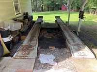 Wide shot of the two rusty metal vehicle ramps side by side under a shelter, showing overall condition and surroundings.