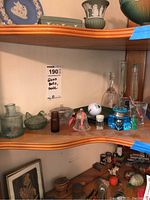 Shelf with various glass items including bells, bottles, blue decorative bottle, shot glasses, and other trinkets.