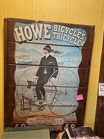 Full view of the Howe Bicycles and Tricycles wooden sign showing a man riding a vintage bicycle with text and branding.