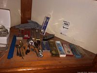 Wide shot of all spoons on wooden surface, some in boxes, some loose, showing variety in designs and packaging