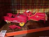 Photo showing two vintage tin fire trucks, one with detached wheels in front