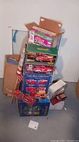 Stack of boxes containing Kellogg's Raisin Bran cereal box, model toy vehicle boxes, and multiple rolled flags, with two toy fire trucks displayed on the floor.