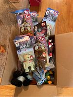 Box containing multiple TY Beanie Babies in original packaging and loose inside, showing Britannia, Maple, Glory, Erin figures.