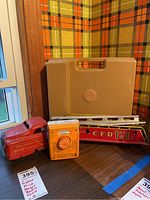 Vintage Fisher Price toy record player, small orange and white toy radio, and red metal fire truck with ladder, displayed together on a table.