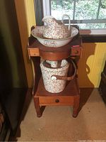 Frontal view of the full wash stand with ceramic basin, pitcher, and pail arranged on it.