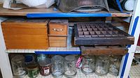 Photo showing a large wooden box, a small wooden box with a drawer, and a segmented wooden tray on a shelf above several glass jars.