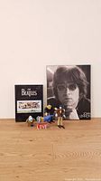 Photo showing the full Beatles set including John Lennon print, Anthology book and Beatles toys arranged on wood floor.