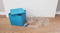 Full set including large bowl, small bowls, serving spoons and box placed on wooden floor.