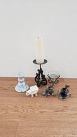 Front view of all six items arranged on a wooden surface showing a variety of candle holders and the small white elephant figurine.