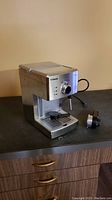 Saeco Poemia espresso maker angled view with power cord visible and portafilter placed beside it on counter.