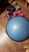Overall view of the exercise equipment items spread on floor including balance ball, dumbbells, jump ropes, roller and spray bottle.