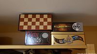 Four boxed games on a shelf: wooden chess/checkers set, Dirty Minds card game, Deal or No Deal DVD game, The Movie Trivia 2 game.
