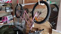 Upside down pink kids bike with knobby tires hanging in garage/storage area, showing frame, wheels, and pedals in good condition