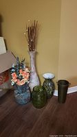 Set of five large decorative vases arranged on wooden floor against beige wall.
