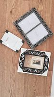 Three metal picture frames on a hardwood floor, showing diverse styles and sizes
