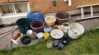 Photo showing a variety of planters and plant pots arranged outdoors on grass and concrete.