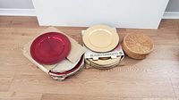 Photo showing multiple stacks of red plate chargers, gold plate chargers with 'Beaded Chargers' label, and vintage rattan chargers on wooden floor.