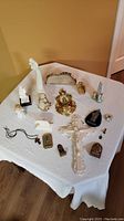 Overview of all religious items on white cloth-covered table including crucifix, statues, plaques, and rosary