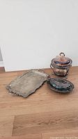 Silver tray, food warmer, and platter arranged on wooden floor against white wall