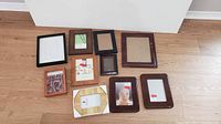 Top-down view of ten assorted wood picture frames on hardwood floor showing various sizes, colors, and conditions.