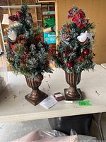 Two artificial Christmas tree planters displayed side by side on a table, showing entire trees and planters.