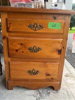 Front view of the wooden bedside table showing three drawers and signs of wear on the top surface.