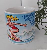 Front view of ceramic mug showing blonde female surfer in red swimsuit with blue background and text.