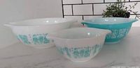 Three Pyrex Amish Butterprint mixing bowls shown side by side, two white base with turquoise print and one turquoise base with white print.