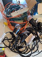 Photo of seven black strobe lights with clear covers and attached power cords tangled with extension cords and cream power bar.
