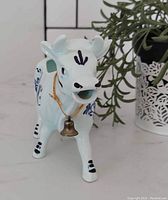 Front angle view of ceramic Delft cow creamer with bell on cord around neck, blue floral decoration.