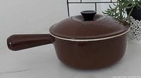 Chocolate brown Le Creuset sauce pan with lid, side view showing handle and lid knob.