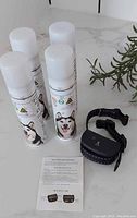 Three white cans of citronella spray with husky image and black ultrasonic bark deterrent collar with adjustable strap, instruction sheet on marble countertop.