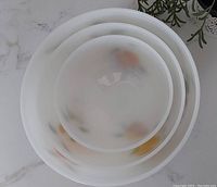 Top view of three nested white milk glass bowls with visible fruit designs underneath