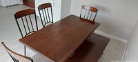 Wooden harvest-style dining table, bench, and 4 chairs arranged in a room