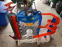 Photo showing the full Hot Wheels Ultimate Garage with orange spiral ramp, vertical lift, central blue turntable, and multiple garage levels