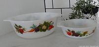 Two JAJ Pyrex Tuscany pattern casserole dishes featured side by side showing vegetable print on the sides and spouted edges.