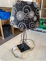 Black metal table lamp with black and white floral patterned fabric shade, showing base and cord.