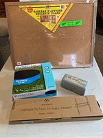 Photo showing cork bulletin board, Bestway pool cover box, gray box with European adapters, and Perlesmith TV wall mount box.