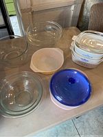 Photo showing set of glass mixing bowls, white opaque bowl, CorningWare casserole dishes, and a blue glass lid on a table.