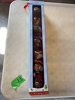 Full view of the box containing 7 vertically aligned ornaments with colored ribbons for hanging.