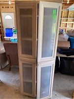 Front view of the beige plastic storage cupboard showing four doors with vertically ribbed panels, overall dimensions noted on a green tag on upper right door.