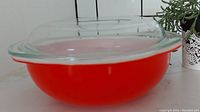 Side view showing red/orange casserole bowl with clear glass lid on top