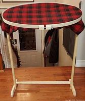 Full view of the white oval hardwood hoop mounted on wooden adjustable floor stand, fabric stretched on hoop is red tartan/plaid pattern.