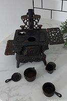 Front top angle showing Resgent miniature stove with fry pan, bucket, kettle accessories around.