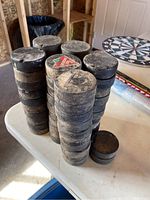 Photo showing stacks of 52 used hockey pucks with some dust and wear marks, arranged on a table.