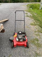 Front view of the red Yard Machines push lawn mower with handlebar and wheels, placed on gravel.