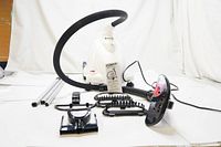 Full view of all components including steamer base unit, flexible hose, pole parts, and multiple black plastic attachments for fabric steaming.